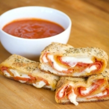 Three Slices of Pepperoni Bread Stacked Next to a Bowl of Marinara Sauce